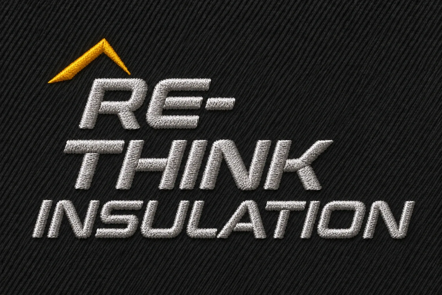 Stickansicht des RE-THINK INSULATION Schriftzugs in hellem Metallic-Silber mit gelbem Dach auf anthrazitfarbenem Textil.